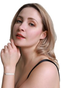 Bracciale d'argento con un charm ovale, catena delicata e piccole pietre decorative. Il modello ha la pelle chiara e capelli biondi ondulati, indossa un top nero.