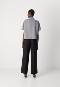 Gray short-sleeve cropped shirt with a back seam detail, paired with high-waisted black wide-leg trousers and black heels.