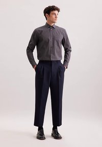 Camicia a fantasia in bianco e nero con colletto, abbinata a pantaloni blu navy a vita alta e scarpe di pelle nere. Tessuto liscio, design aderente.