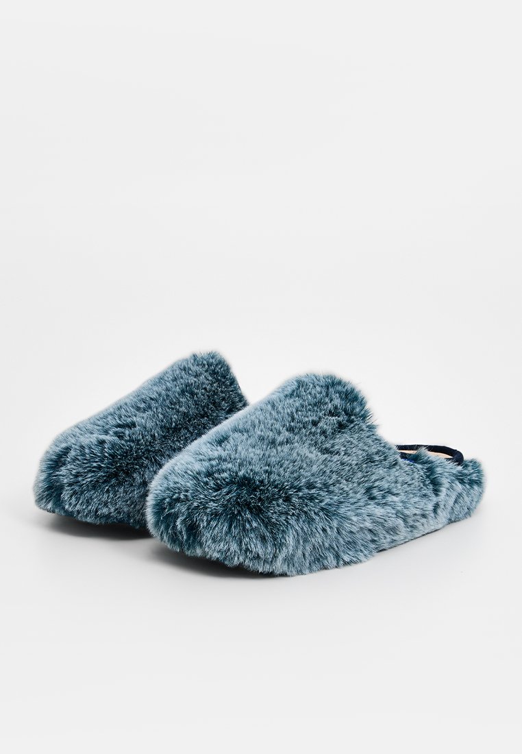 Pantofole morbide e pelose di color verde scuro, caratterizzate da una forma arrotondata e una texture soffice, progettate senza chiusure visibili.