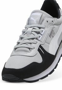 Scarpa sportiva grigia e nera realizzata in mesh e suede, con una spessa suola bianca, lacci e logo Puma sulla linguetta e sul lato.