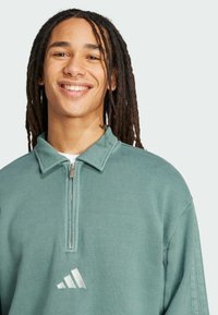 Grön kvart zip sweatshirt gjord av mjukt material, med krage, silverfärgad logotyp på bröstet och avslappnad passform.