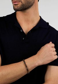 Braccialetto di perline con pietre rotonde e levigate in tonalità di marrone e nero, su una pelle dalla texture definita, indossato al polso.