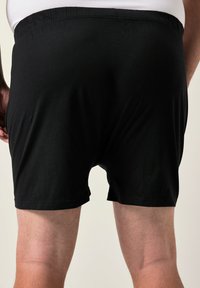 Pantaloni corti neri in cotone con vita elasticizzata, con una texture liscia e senza motivi o dettagli visibili. Vista posteriore mostrata.