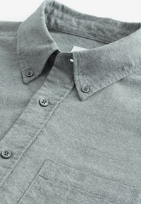 Grå button-up skjorta gjord av mjukt, texturerat tyg. Har en spridd krage, två knappar och en bröstficka.