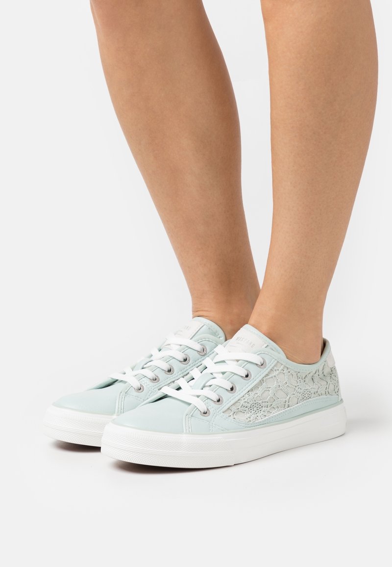 Světle modré plátěné tenisky s tkaničkovou panele, bílé gumové podrážky a ploché bílé tkaničky. Vyznačují se nízkým střihem a texturovaným svrškem.