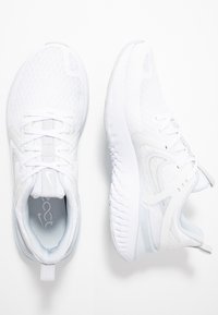 Białe buty sportowe z siateczkową cholewką, teksturowaną podeszwą i sznurowaniem. Posiadają dyskretną logo oraz uchwyt na pięcie.