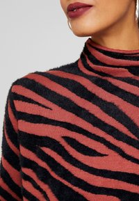 Maglione a collo alto con una base texturizzata ruggine e audaci strisce zebrate nere pelose. Il tessuto appare morbido e caldo.