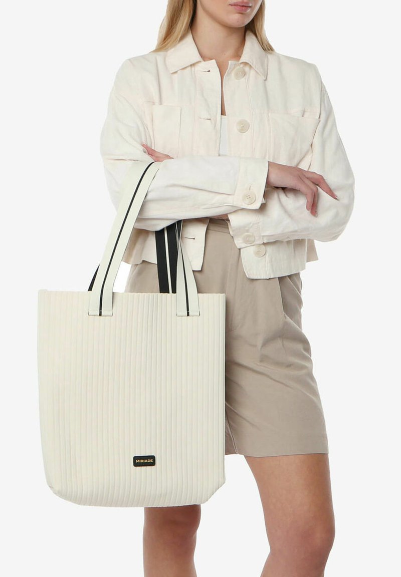 Borsa tote bianca a coste con manici rigati in bianco e nero, caratterizzata da un'etichetta nera con logo alla base. La borsa ha una forma strutturata e una superficie texturizzata.