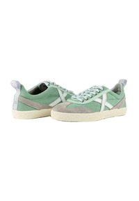 Zapatillas de lona verdes con acentos de ante gris. Presentan costuras blancas y una suela texturizada de color crema. Incluyen cordones planos y una pestaña de refuerzo en el talón.