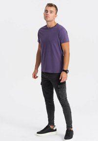 Lilla kortærmet t-shirt, parret med sorte slim-fit jeans og sorte sneakers. Simpelt design med glat tekstur og ingen synlige mønstre.