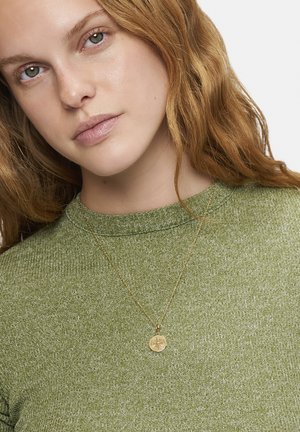 Goldfarbener, runder Anhänger-Halskette an einer feinen Kette, getragen über einem grünen, strukturierten Pullover mit rundem Halsausschnitt.