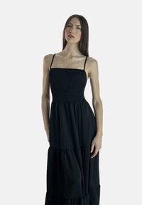 Sort maksi kjole med en smocket bodice, tynde stropper og lagdelt flæsekanter. Stof ser blødt ud og har en subtil tekstur over det hele.