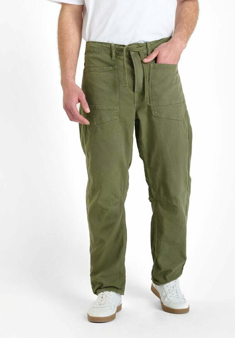 Man in olijfgroene cargobroek met grote voorkruikezakken en een strikceintuur, gecombineerd met witte sneakers en een wit shirt.