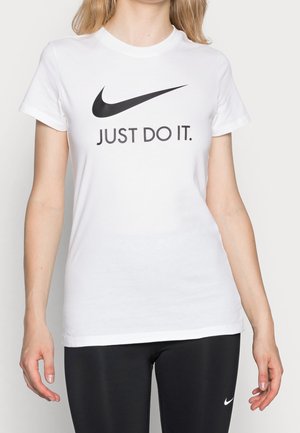 Kobieta w białej koszulce Nike z czarnym napisem i logo "Just Do It.", w połączeniu z czarnymi legginsami Nike.