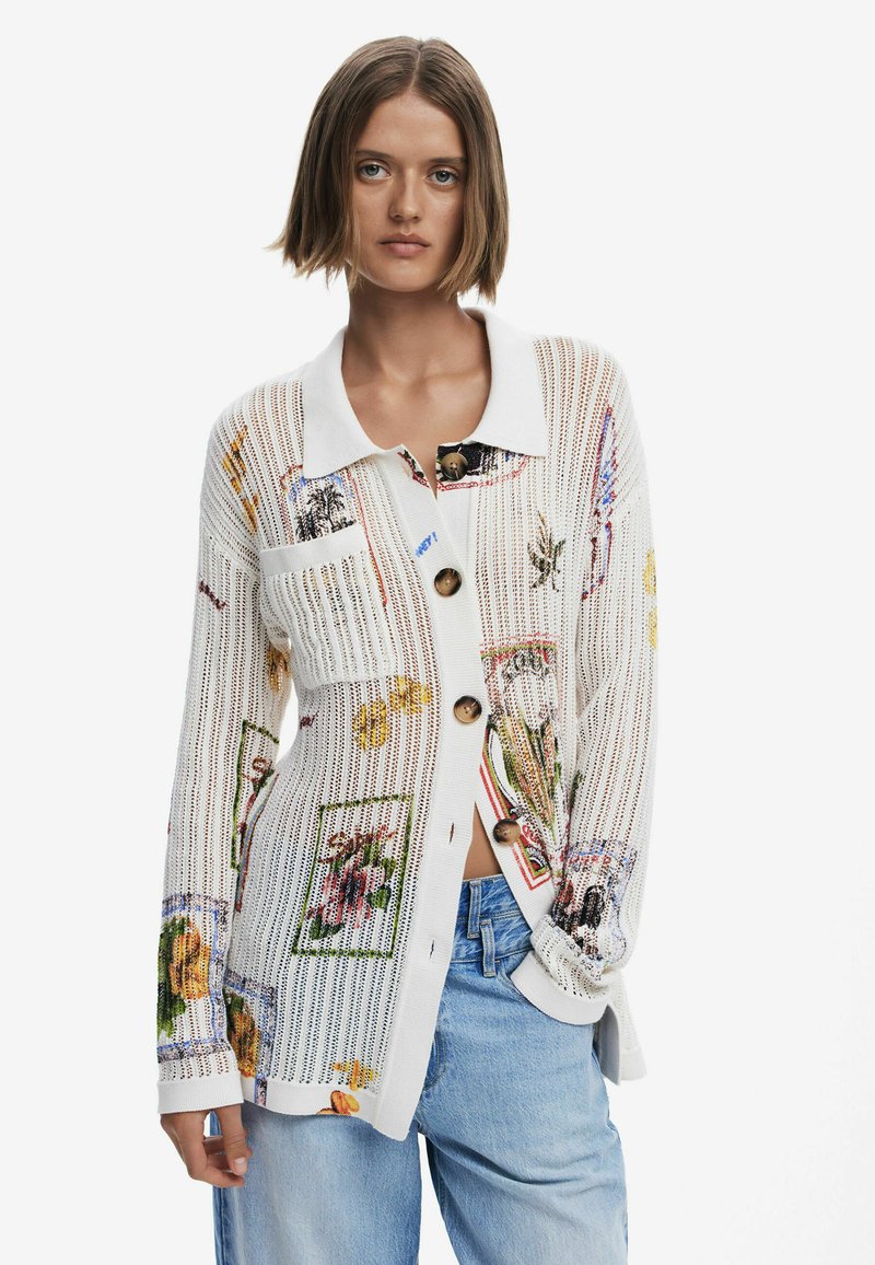 Balta megztinė su spalvingais gėlių raštais; turi apykaklės iškirptę, mygtukų užsegimą ir tekstūruotą audinį. Atsitiktinis siluetas su kišenėmis.