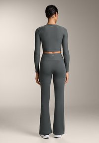 Szürke bordázott hosszú ujjú crop top, magas derekú harangszárú nadrággal párosítva. Az anyag rugalmasnak tűnik, sima textúrával és diszkrét logóval a hátán.