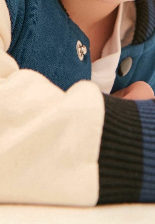 Personne portant une veste bleue et blanche avec des boutons-pression, reposant son bras sur une surface claire.