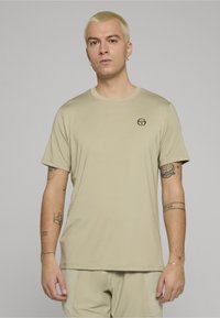 Béžové tričko s krátkými rukávy a kulatým výstřihem, s malým černým logem na hrudi. Hladká látka, volný střih.