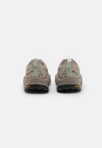 Chaussures de trail légères en beige avec une tige texturée, dotées d'une languette verte et d'une semelle extérieure Vibram pour une meilleure adhérence et durabilité.