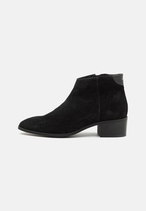 Black suede ankle boot with a pointed toe, low block heel, and minimalistic design. Features a small logo accent on the back.