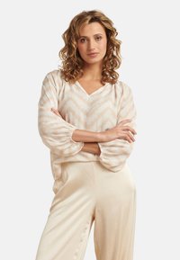Cream-colored blouse with a V-neck, balloon sleeves, and a zigzag pattern. Paired with light beige, loose-fitting trousers.