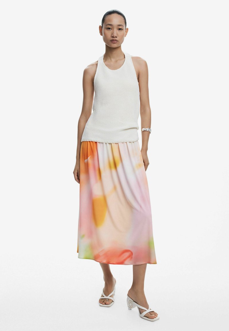 Top din tricot alb cu decolteu halter, asortat cu o fustă maxi vaporoasă, multicoloră, cu un model în pasteluri și sandale cu toc albe.
