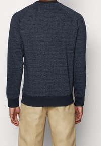 Marineblaues Fleece-Sweatshirt mit strukturiertem Muster, gerippten Bündchen und Saum sowie einem runden Halsausschnitt. Rückansicht mit Details zu den Ärmeln und Passform.