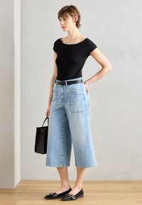 Svart tettsittende t-skjorte, lyseblå vide avkuttede jeans med lommer, svart belte, svarte leppestift med utsmykninger, og en liten svart håndveske.