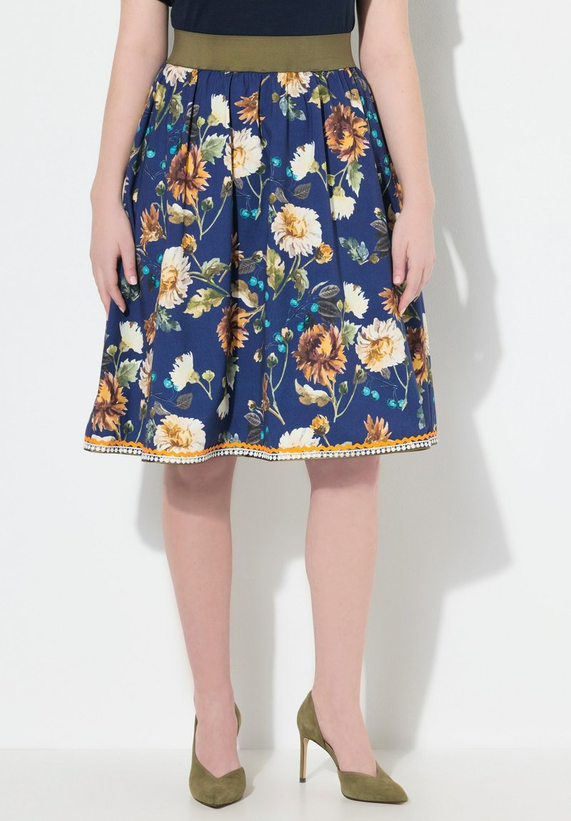 Kukallinen hame, jossa on tummansininen tausta, kirkkaat keltainen ja valkoinen kukkakuosi, tiukka vihreä vyötärö ja koristeellinen reuna helmassa.