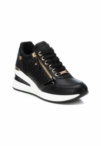 Zapatilla negra con textura acolchada, acentos de herrajes dorados y un cierre lateral. Presenta una suela de cuña con un diseño en bloques de color blanco y negro.