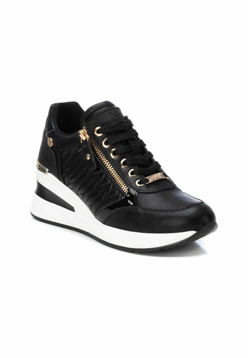 Zapatilla negra con textura acolchada, acentos de herrajes dorados y un cierre lateral. Presenta una suela de cuña con un diseño en bloques de color blanco y negro.