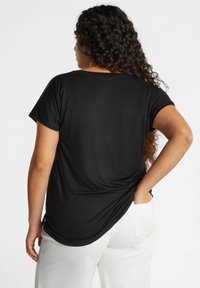 Sort kortærmet t-shirt med rund halsudskæring, afslappet pasform og draperet tekstur, parret med hvide bukser.