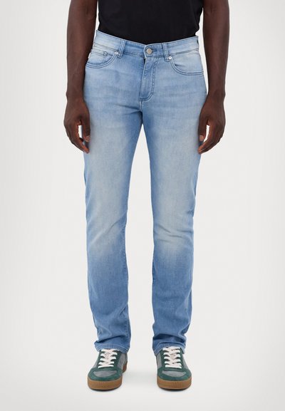 Jean en denim bleu clair avec une coupe droite, cinq poches et une légère décoloration. Associés à des baskets vertes et blanches avec des lacets et une semelle texturée.