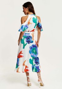 Floral-patterned, cold-shoulder dress with ruffled sleeves, predominantly white, featuring vibrant green, blue, and orange accents.