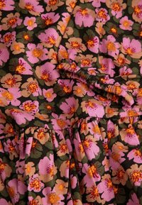 Kwiatowa tkanina w odcieniach różu, pomarańczy i zieleni na ciemnym tle. Posiada fałdy oraz teksturowaną, prążkowaną powierzchnię.