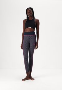 Svart crop topp med hvitt logo og mønstrede marineblå leggings med rosa detaljer og figurnær design, laget av stretchstoff.