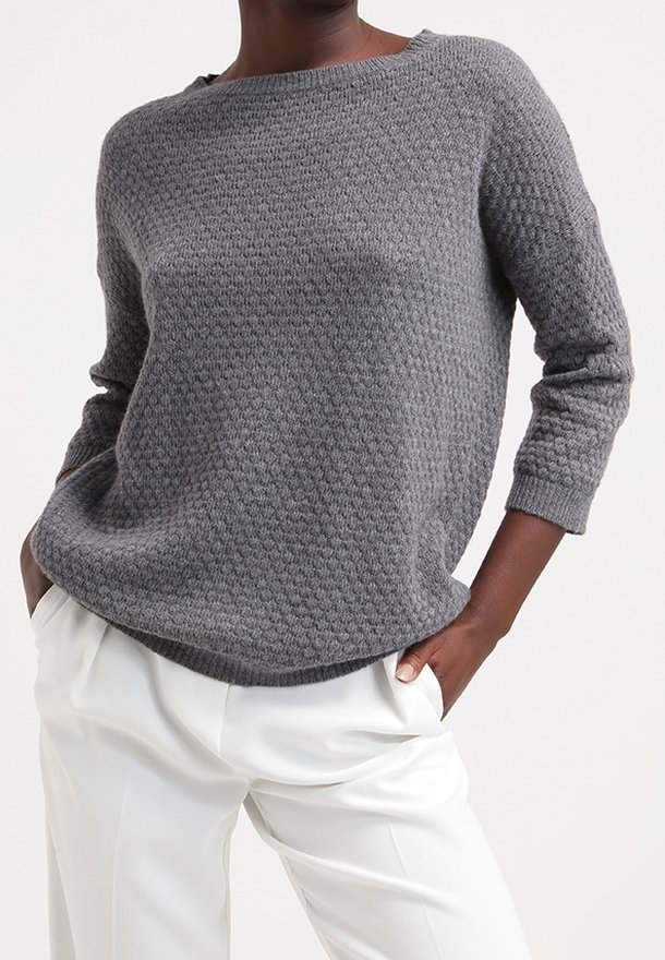 Pull en tricot gris avec un motif texturé, encolure bateau et manches trois-quarts, associé à un pantalon blanc.