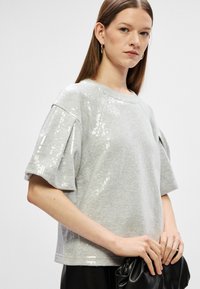 Hallus halli lühikeste varrukatega topp, mille ühel küljel on sädelevad litrid, ümmargune kaelus ja lõtv istuvus. Tekstureeritud kangas, millel on pehme välimus.