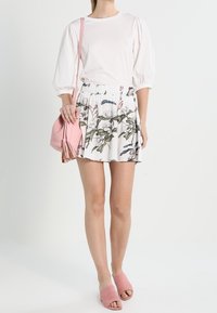 Vit topp med puffärmar matchad med en vit blommig kjol med gröna och rosa accenter. Accessoarer med en rosa väska och matchande sandaler.