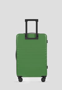 Groene harde koffer met een gestructureerd, ribbelachtig oppervlak, hertracteerbaar zwart handvat en vier wielen voor mobiliteit.