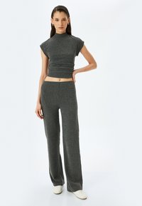 Grå ribbet crop top med høj hals og korte ærmer, parret med matchende højtaljede bukser med bred ben. Enkle hvide sneakers.