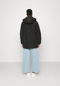 Svart vadderad jacka med huva, med strukturerad yta och synliga sömmar, ihop med ljusblå vida jeans och vita sneakers.
