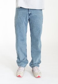 Jean droit bleu clair en denim, doté d'une taille visible et de détails de couture subtils, associé à des chaussures de sport blanches.