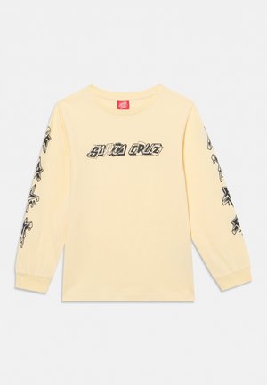 Chemise jaune clair à manches longues avec le texte "Santa Cruz" sur la poitrine et des motifs d’étoiles noires dégoulinantes le long des deux manches.