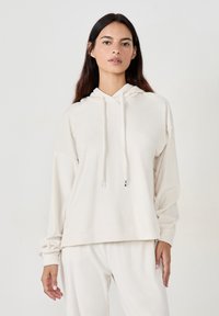 Cremfarbener Hoodie aus weichem Stoff, mit Kordelzugkapuze, lockerer Passform und gerippten Bündchen. Das Design ist minimalistisch und nahtlos.