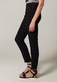 Svarta mönstrade byxor med slim fit, med en texturerad design och hög midja. Matchade med svarta sandaler med remmar.