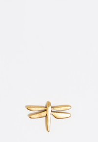 Broche de libélula de color dorado con un acabado texturizado, que presenta cuatro alas alargadas y un cuerpo redondeado. Diseño minimalista sobre un fondo blanco.