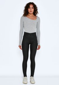 Grijze lange mouwen top van ribbelstof, gecombineerd met zwarte hoge skinny jeans. Subtiele details en een soepele textuur, met witte sneakers.