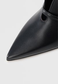 Μαύρο δερμάτινο παπούτσι μυτερό στη μύτη με ομαλή υφή και λεπτομέρεια κοπής στο πλάι, με λεπτή σόλα και μινιμαλιστικό σχέδιο.